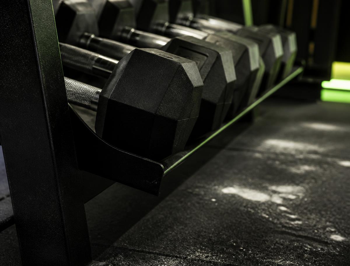Close-up of a rack of black hex dumbbells in a dimly lit gym